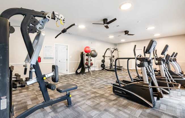 A gym with a variety of equipment including treadmills, weights, and a bench.