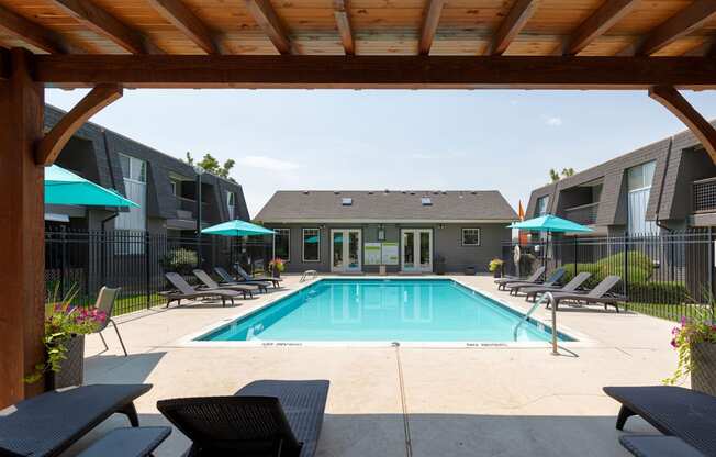 A pool area with a wooden pergola and lounge chairs.