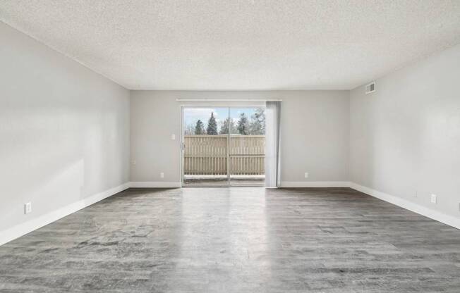 A large empty room with a view of a fence and trees outside the window.