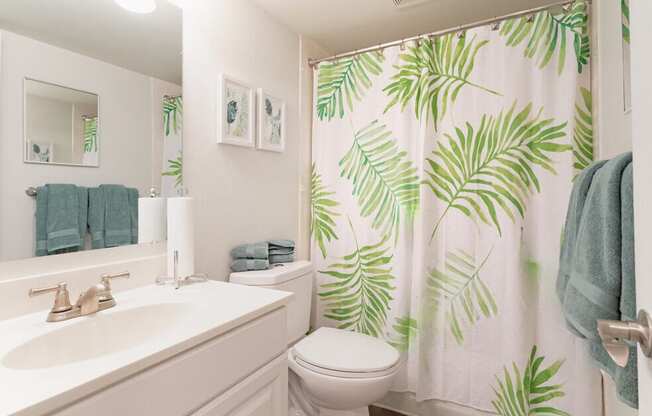 A bathroom with a white sink, toilet, and a green leafy shower curtain.