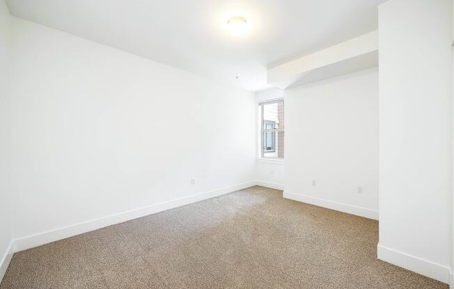 a living room with white walls and carpet and a window