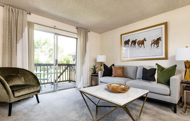 A living room with a grey couch, a green chair, and a painting of horses on the wall.