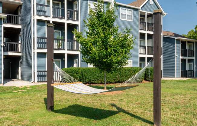 a hammock sits in the grass in front of an apartment building