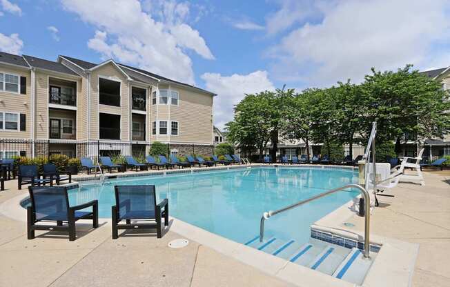 A swimming pool surrounded by chairs and trees in front of a building.