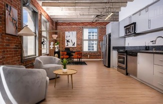 an open living room with a kitchen and a exposed brick wall