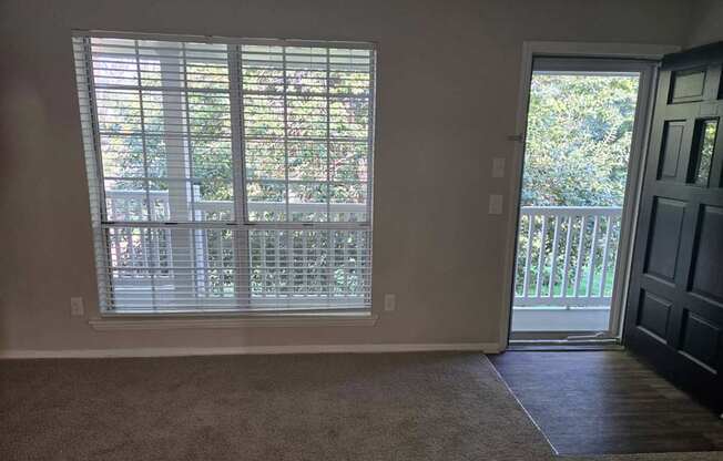 A room with a carpeted floor, a sliding glass door, and a wooden door.
