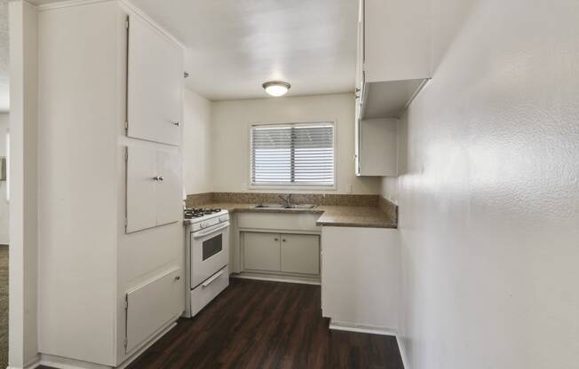 Kitchen with white gas range,  granite countertops, white cabinets, and wood-inspired floors