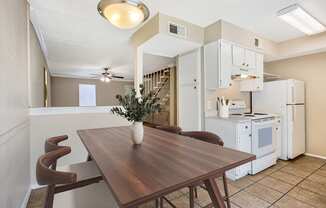 a dining room with a wooden table and a kitchen with white appliances