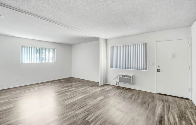 the spacious living room of an apartment with wood flooring and white walls