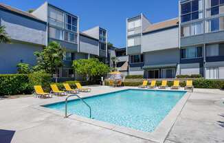 a swimming pool with yellow chairs in front of an apartment building