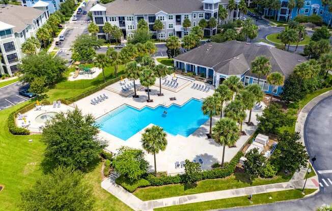 An aerial view of a swimming pool surrounded by palm trees and a building.