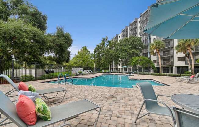 A pool surrounded by chairs and trees with a building in the background at Hampton Apartments, Clearwater