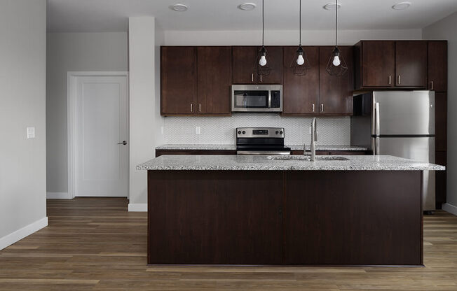 a kitchen with a large island with granite countertops and dark wood cabinets