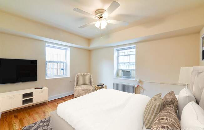 bedroom with bed, dresser, tv, seating area with windows and ceiling fan at 4031 davis place apartments in washington dc