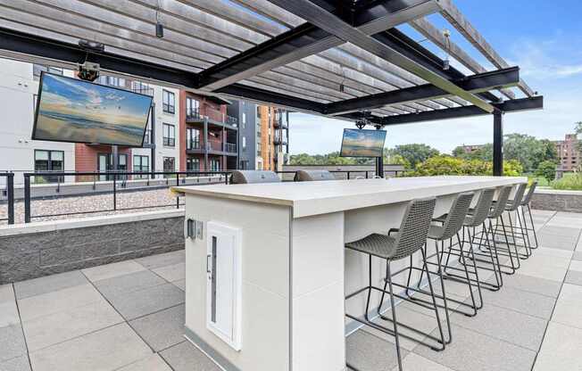 A patio with a bar and chairs under a roof.