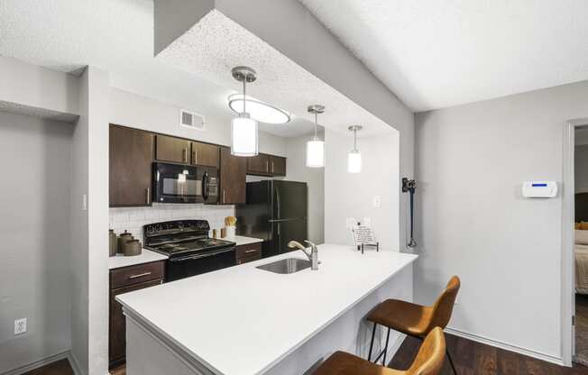 a kitchen with a white counter top and a white island with a sink and two chairs