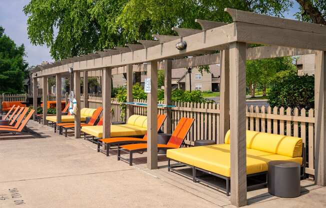 a row of orange and yellow lounge chairs under a wooden pergola