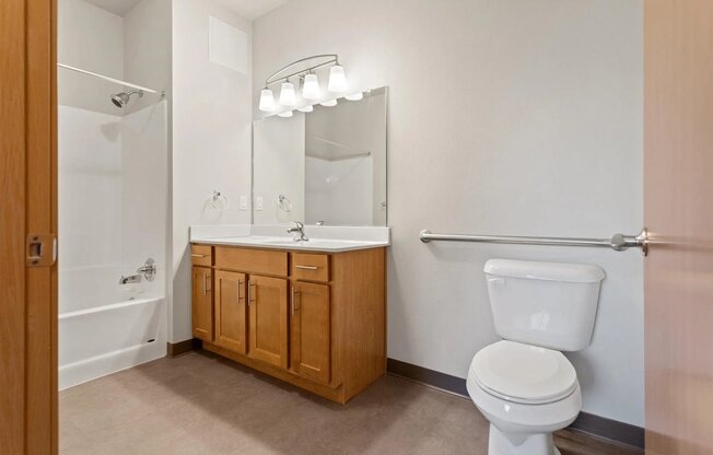 a bathroom with a sink vanity with mirror and lights, a toilet, and a shower/tub