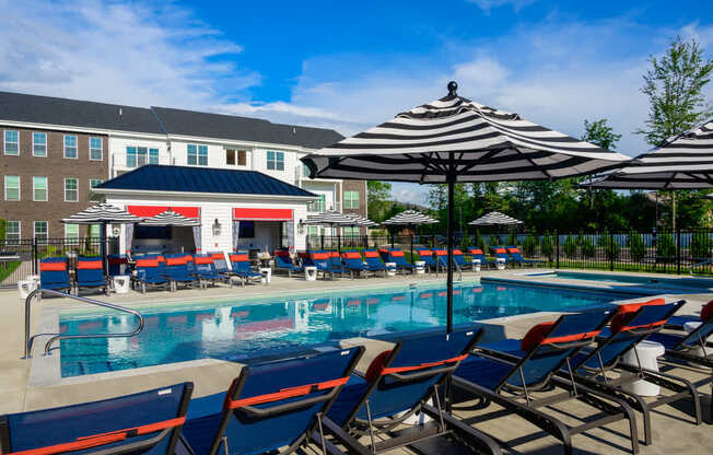 A pool area with sun loungers and umbrellas in front of a building.