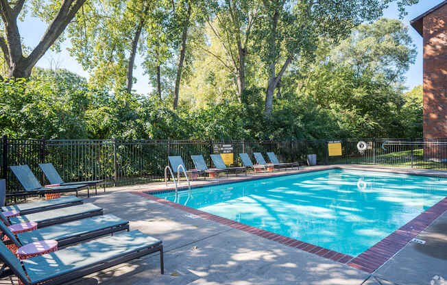 a swimming pool with lounge chairs and trees in the background