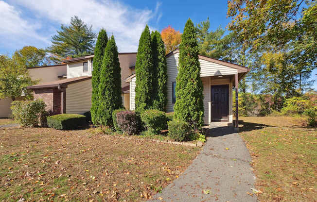 A house with a grey roof and a brown door is surrounded by trees and bushes.