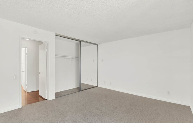 an empty living room with white walls and sliding glass doors to a closet at Camino de Oro Apartments, Torrance, California