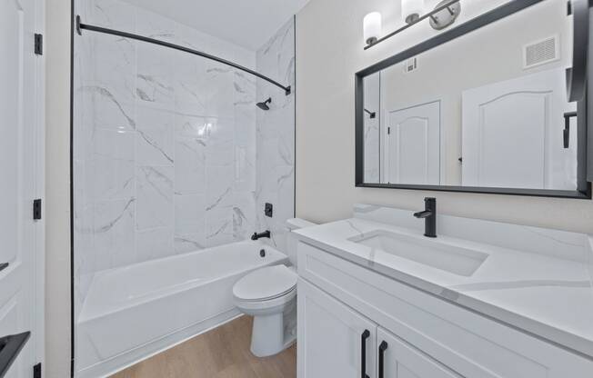 a bathroom with white cabinets and a white toilet next to a white bathtub with a shower