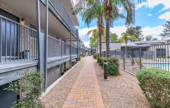 A long brick pathway leads through a landscaped area with a pool and palm trees.