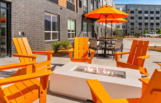 A patio with orange chairs and a fire pit.