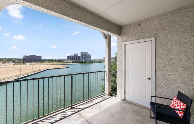 A balcony with a white door and a black chair with a red and white pillow.