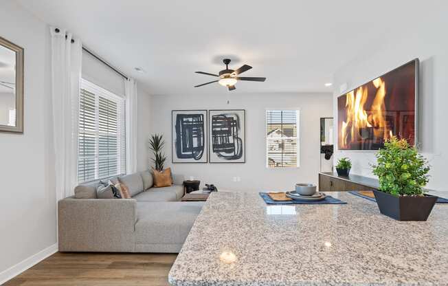 A Sanctuary at Indain Creek model home living room with furnishings, a granite top island, and a ceiling fan