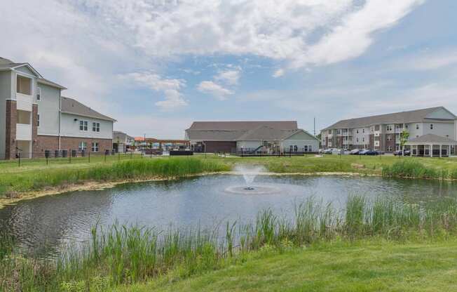 A pond with a fountain with grove city apartments in the background