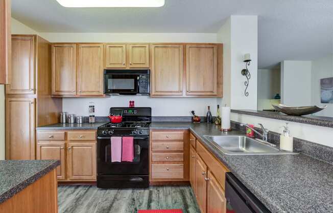 Kitchen with hardwood-style flooring, honey upper and lower cabinets with ample countertop space and black oven with mounted microwave above at Summit Place apartments in Methuen, MA.