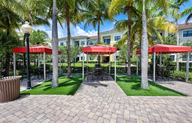 a courtyard with red umbrellas and green grass and palm trees