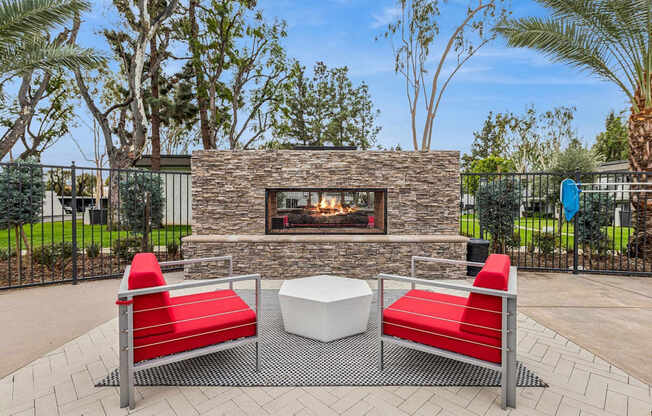 A patio with a stone fireplace, two red chairs and a white table.