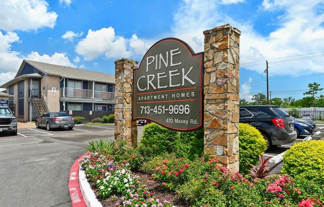 A sign for Pine Creek Apartment Homes stands in front of a building.