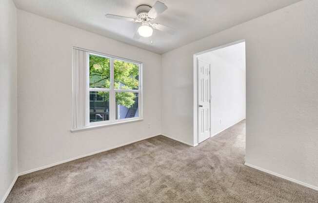 an empty bedroom with a ceiling fan and a window