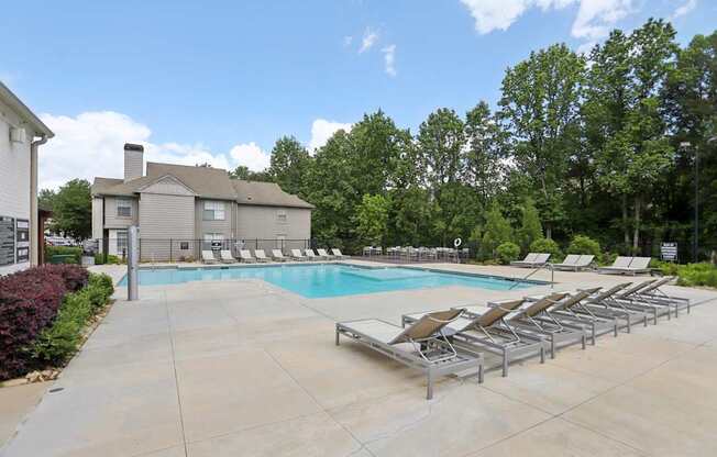 A pool surrounded by lounge chairs and trees.