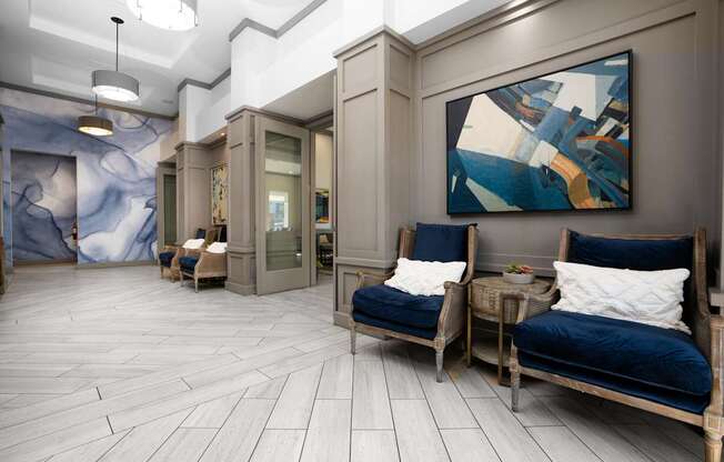 A modern living room with a blue couch and a large abstract painting on the wall.