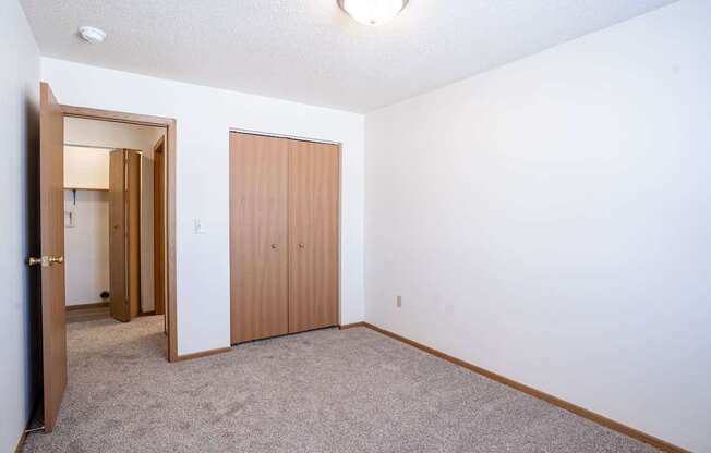 A room with a carpeted floor and a closet. Fargo, ND Country Edge Apartments