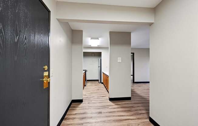 an empty hallway with a black door and white walls and wood floors