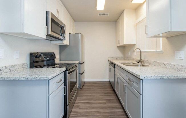 Alternate view of kitchen with stone counters, white cabinets, stainless appliances