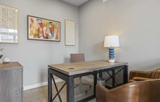 a desk with a lamp and a chair in a room with paintings on the wall,