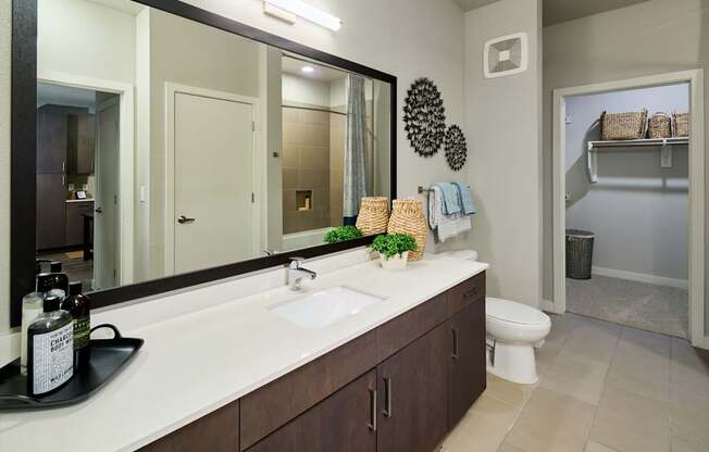 A bathroom with a large mirror, a sink, and a toilet.