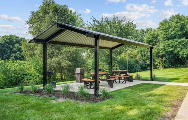 A picnic area with a shelter and benches is surrounded by greenery.