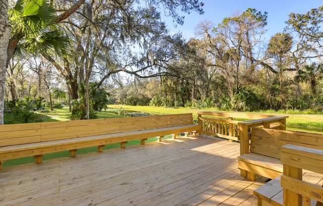 a large wooden deck with benches and trees in the background