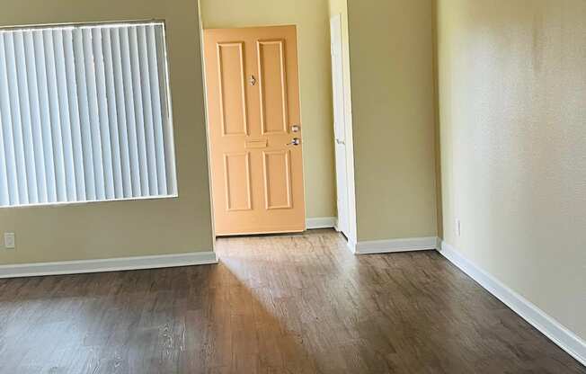 Living room with large window and entry closet with plank style flooring at Plaza Verde Apartments in Escondido, California.