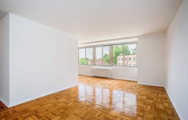 A room with a wooden floor and a window overlooking a building.