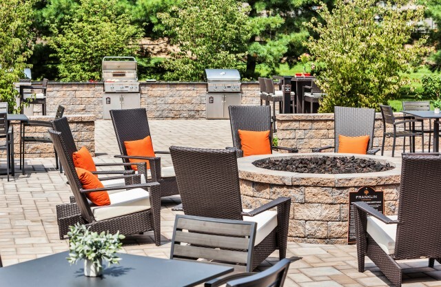 Outdoor fireplace area with comfortable chairs and BBQ grills at Franklin Commons apartments for rent in Bensalem, PA