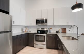 1 Bedroom Apartments In Wheat Ridge, CO - The Parallel - Gourmet Kitchen with White Upper Cabinets and Dark Brown Lower Cabinets, White Tile Backsplash, Quartz Countertops, Stainless Steel Appliances, and Luxury Plank Floors